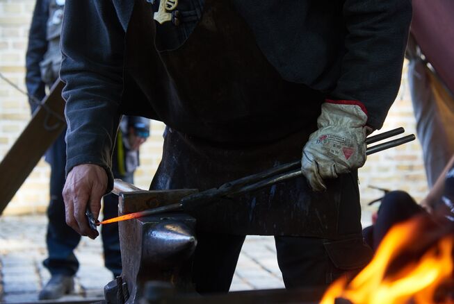 Bild vergrößern: Ein Kunstschmied schleift sein Werkzeug. Im Vordergrund lodert Feuer zum Herstellen von handwerklichen Schmiedekunstarbeiten.